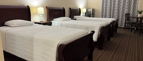 Quarto de hotel com duas camas, uma escrivaninha, uma cadeira, um abajur e uma janela com cortinas.