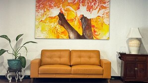 Une pièce avec un grand tableau abstrait au mur, un canapé marron, une petite table avec une lampe et une plante en pot.
