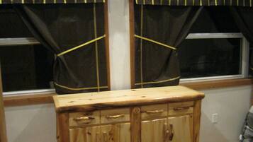 A wooden cabinet with drawers and handles, positioned in front of a window with black curtains tied back with yellow strings.