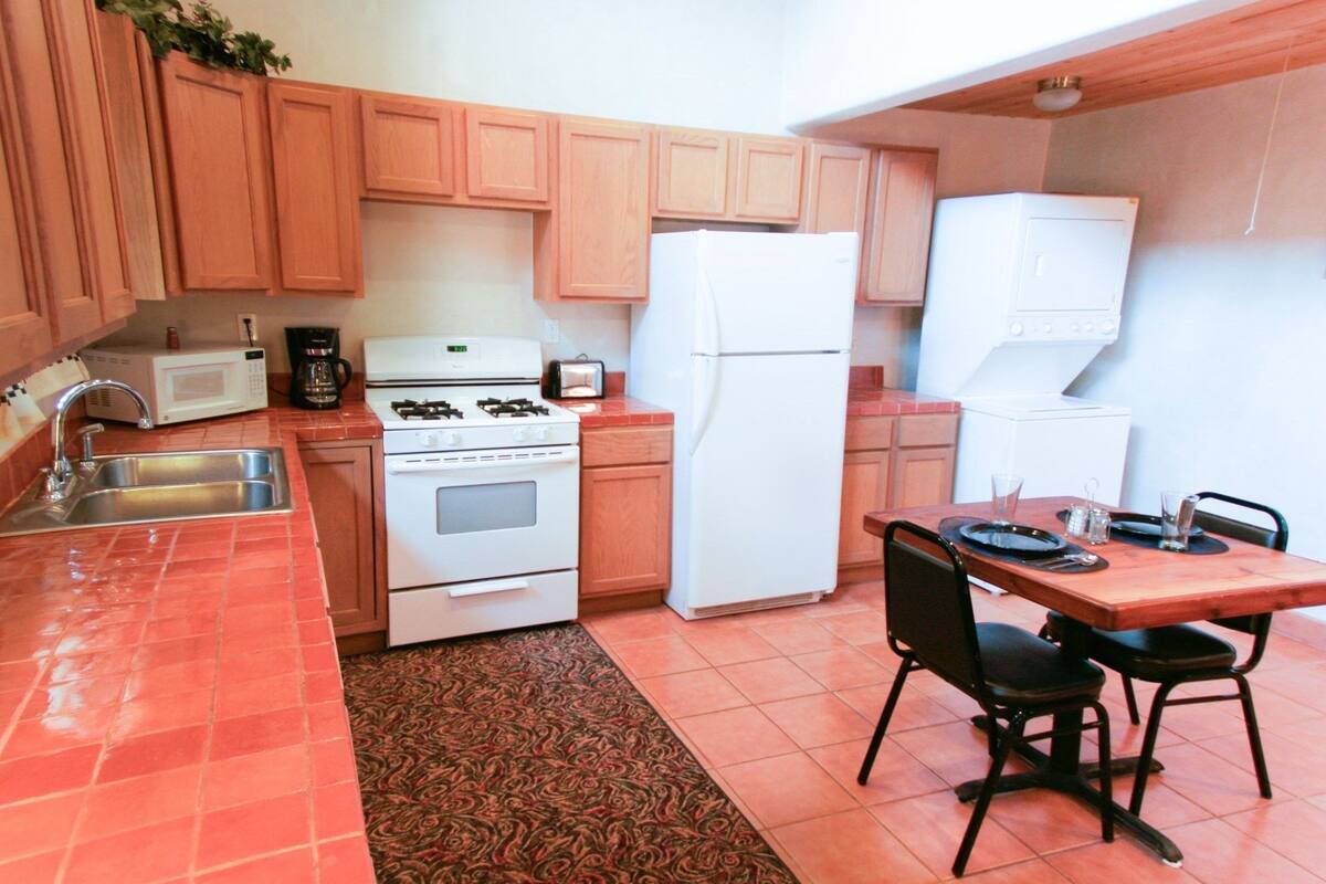 A compact kitchen with wooden cabinets, a stove, a refrigerator, and a dining table with chairs.