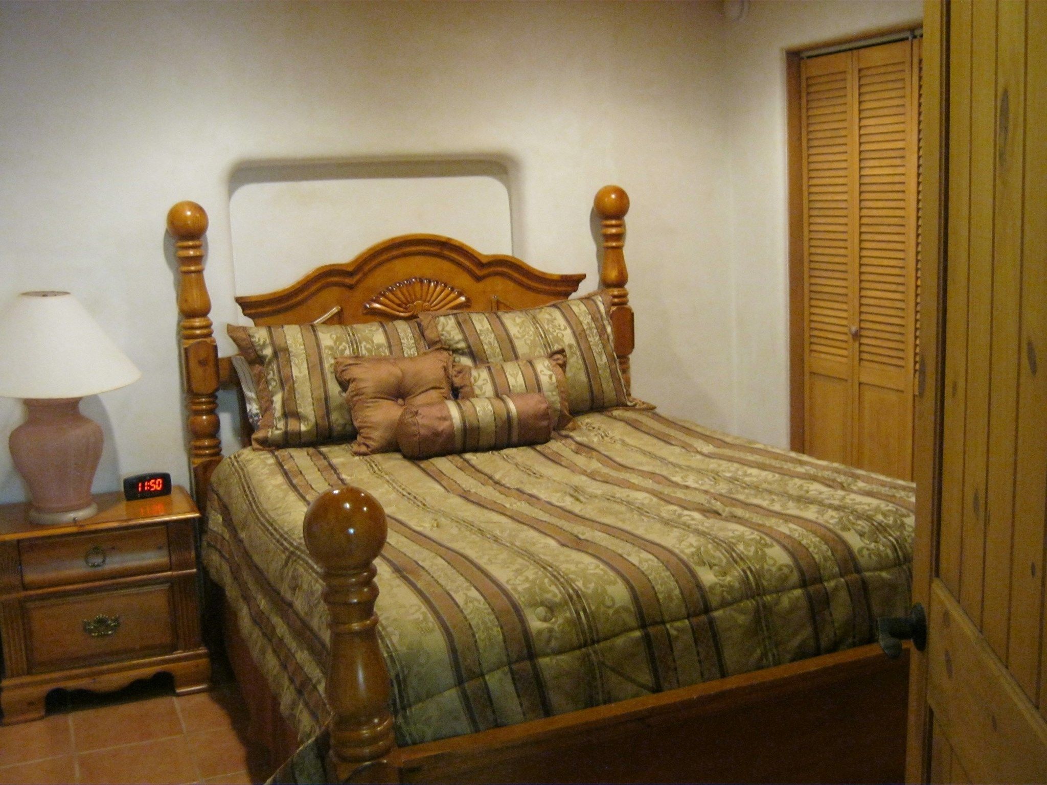 Un dormitorio con una cama de madera, una mesita de noche con lámpara y un armario.