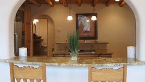 A kitchen with a marble countertop, wooden chairs, a potted plant, and a framed picture on the wall.