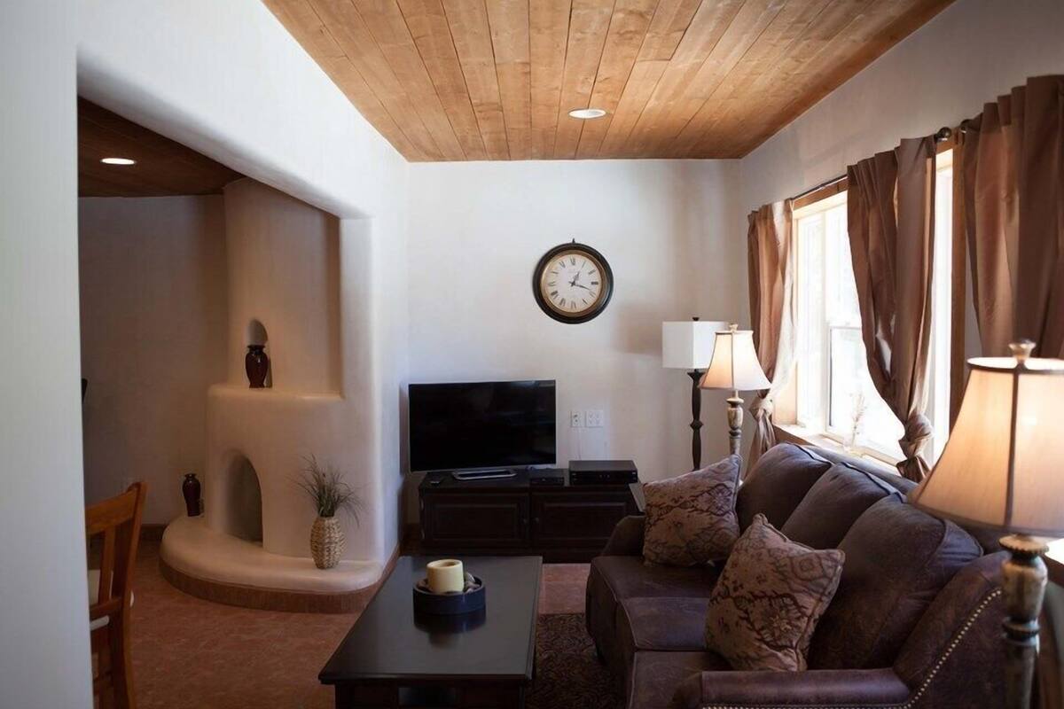 A living room with a wooden ceiling, a flat-screen TV, a sofa, a coffee table, and a lamp.