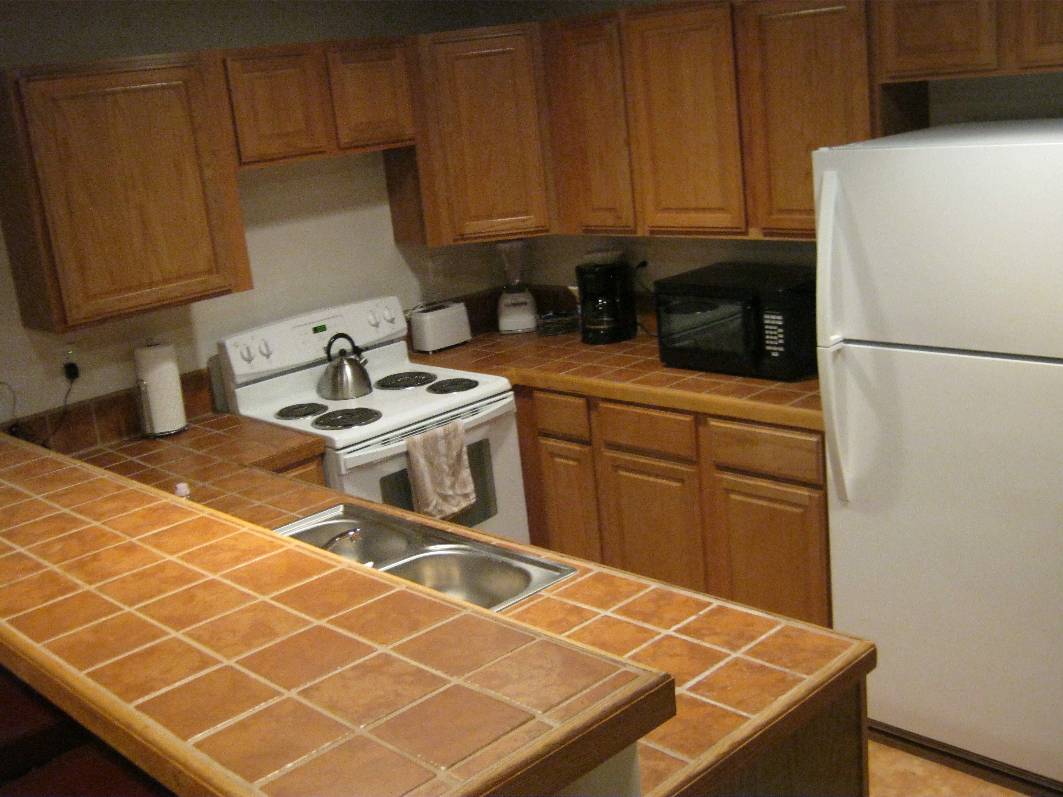 A kitchen with wooden cabinets, a white stove, a microwave, and a refrigerator.