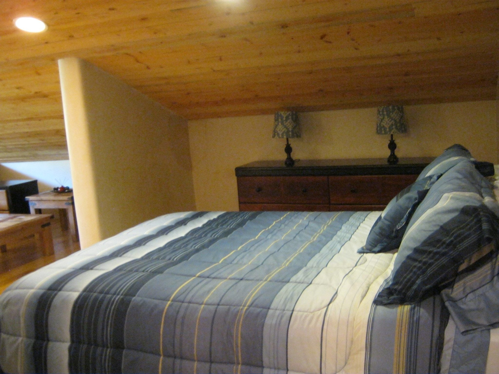 A bedroom with a bed, wooden ceiling, dresser, and nightstands.