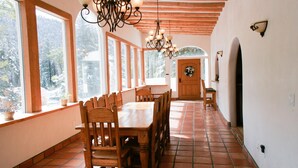 A dining area with wooden tables and chairs, large windows, and a wooden ceiling.