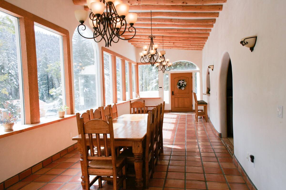A dining area with wooden tables and chairs, large windows, and a wooden ceiling.
