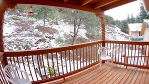 A wooden deck with two white plastic chairs, a railing, and a view of a snowy landscape with trees and a building in the background.