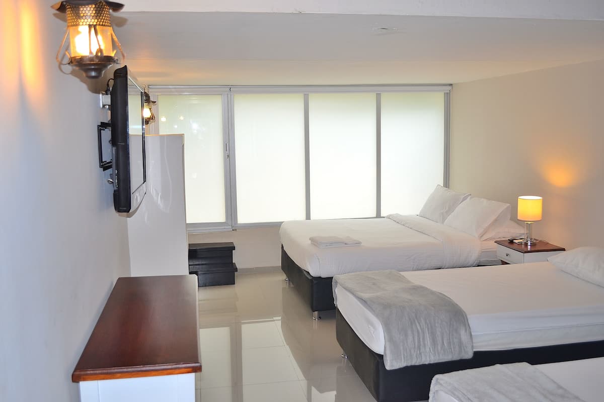 A hotel room with two beds, a desk, a lamp, and a large window with blinds.