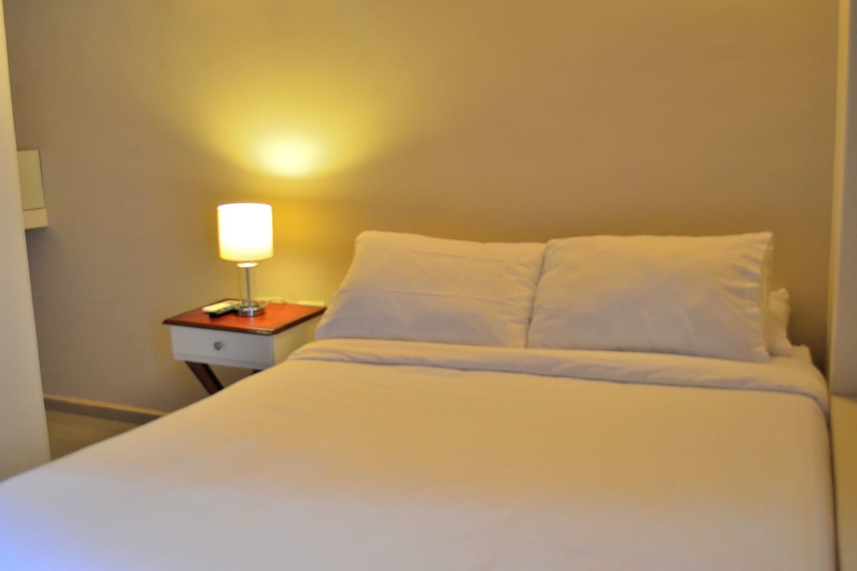 A neatly made bed with white linens in a hotel room.