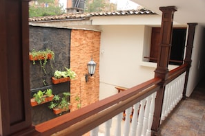 A balcony with a wooden railing, potted plants, a lantern, and a view of a building with a tiled roof. - Hotel Casa La Fleur (Medellín)