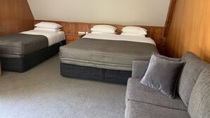 A bedroom with two beds, a wooden headboard, a nightstand, and a grey sofa. - Colonial Motel (Papakura)