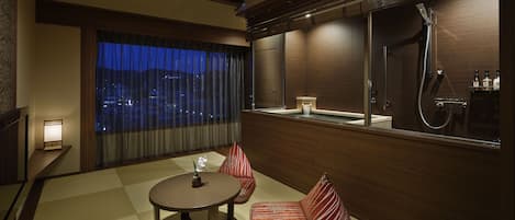 Una habitación de hotel moderna con un ventanal grande, una mesa redonda, un sofá y ducha integrada.