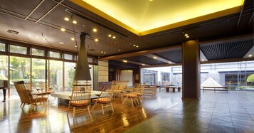 Un espacio interior amplio con suelo de madera, varios conjuntos de asientos y grandes ventanales que dejan entrar luz natural.