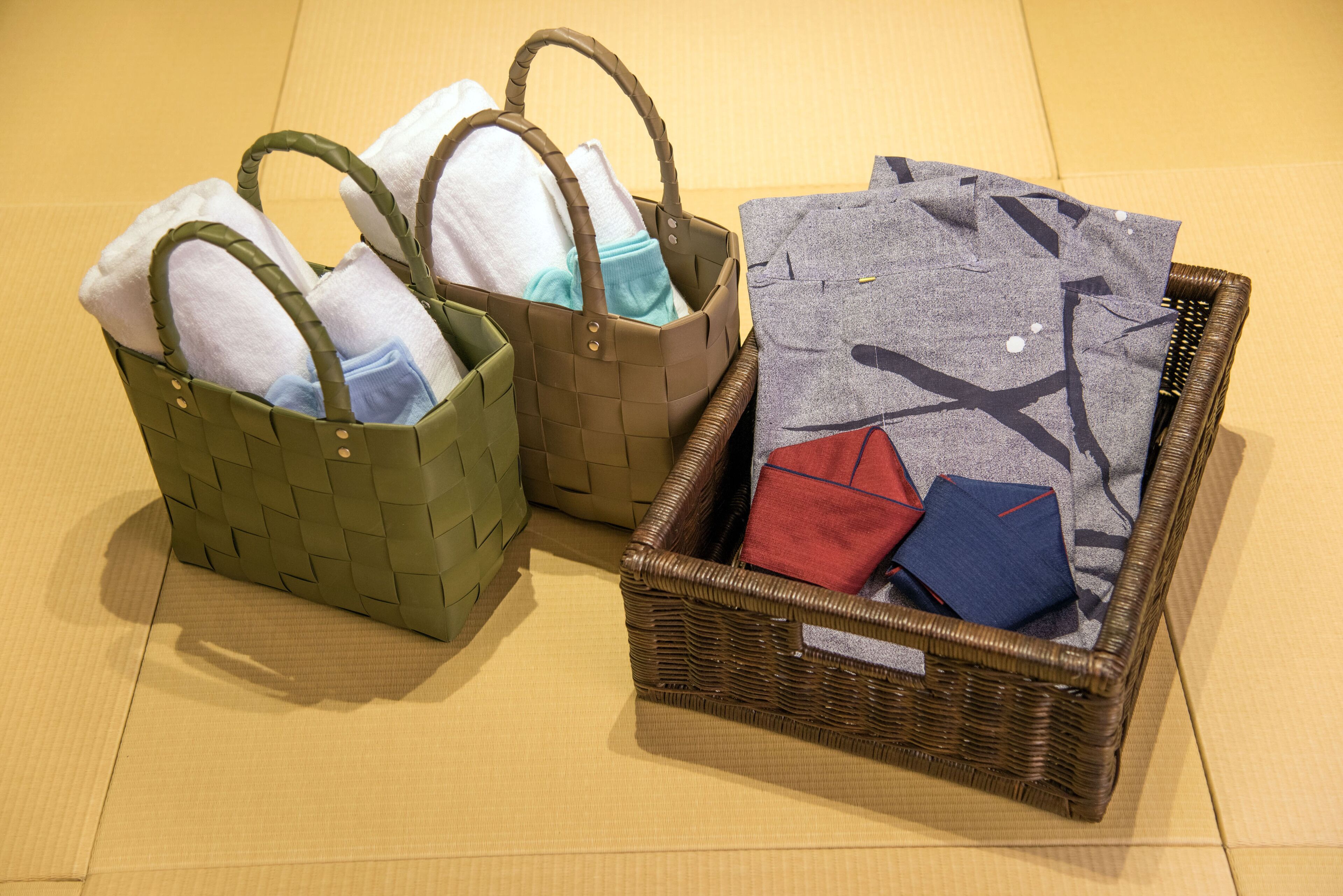 Three wicker baskets with handles, each containing folded towels and a pillow.