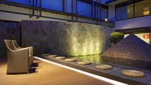 A modern outdoor area with a stone wall, a wooden deck, and a wicker chair. - Laforet Ito Onsen Yunoniwa (Ito)