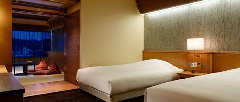 A hotel room with two beds, a wooden headboard, a nightstand, and a window with a view of mountains.