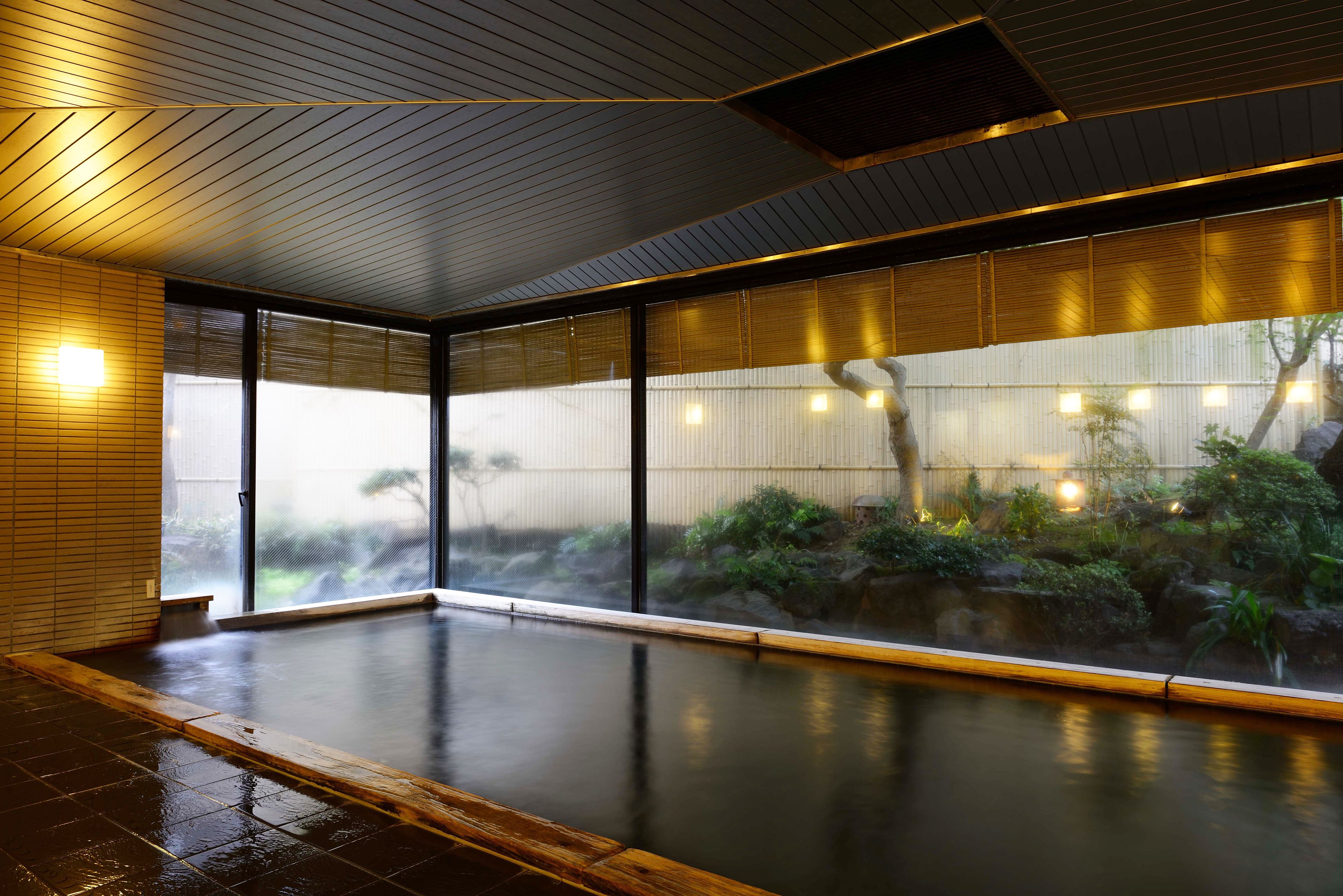 A modern indoor swimming pool with a wooden floor, large windows, and a view of a garden.