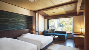 A hotel room with two beds, a sofa, a small table, and a view of the city through large windows. - Laforet Ito Onsen Yunoniwa (Ito)