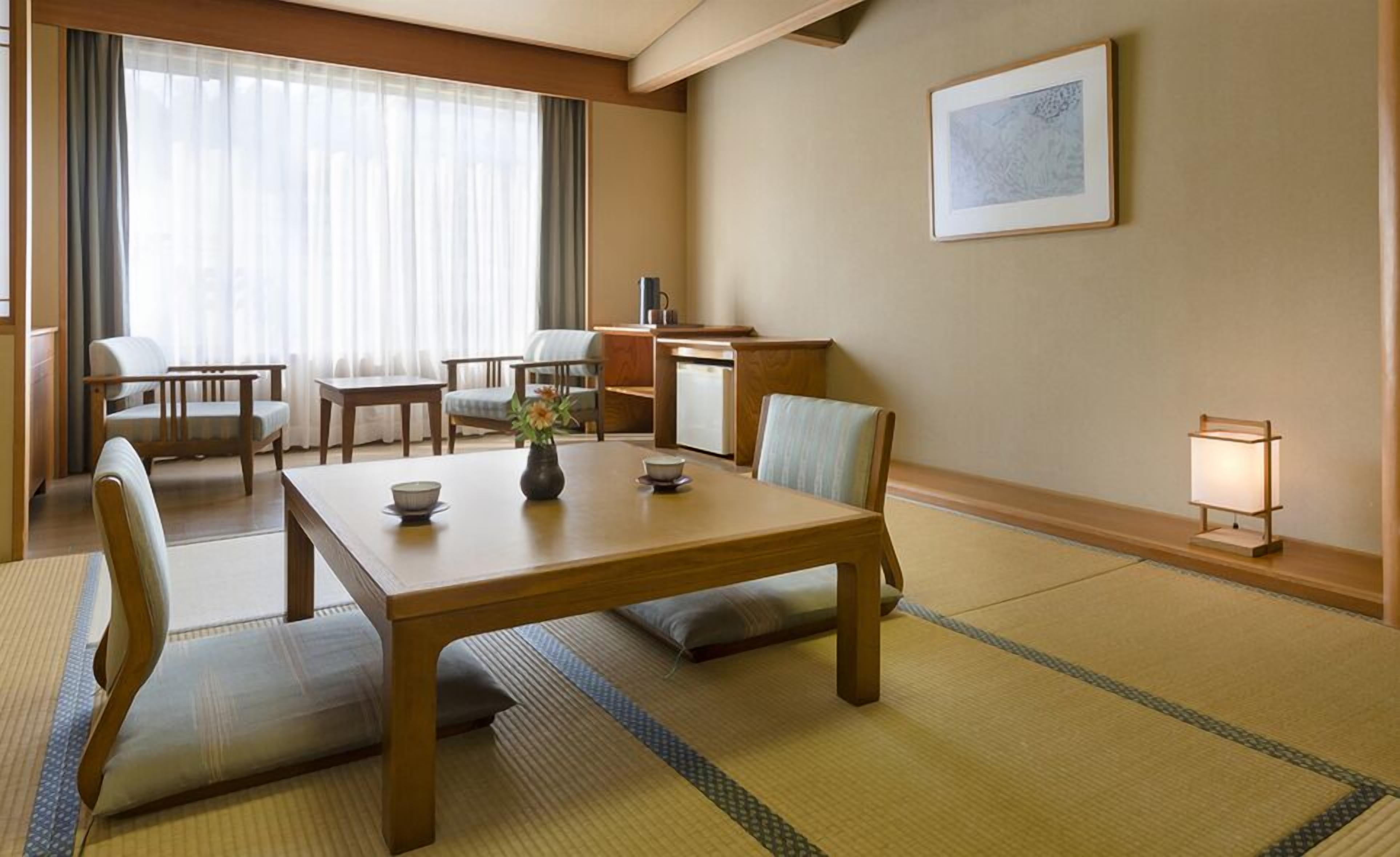 Une pièce de style japonais traditionnel, avec un sol recouvert de tatamis, une petite table sur laquelle sont posés un bol et un vase, et un bureau avec une lampe.