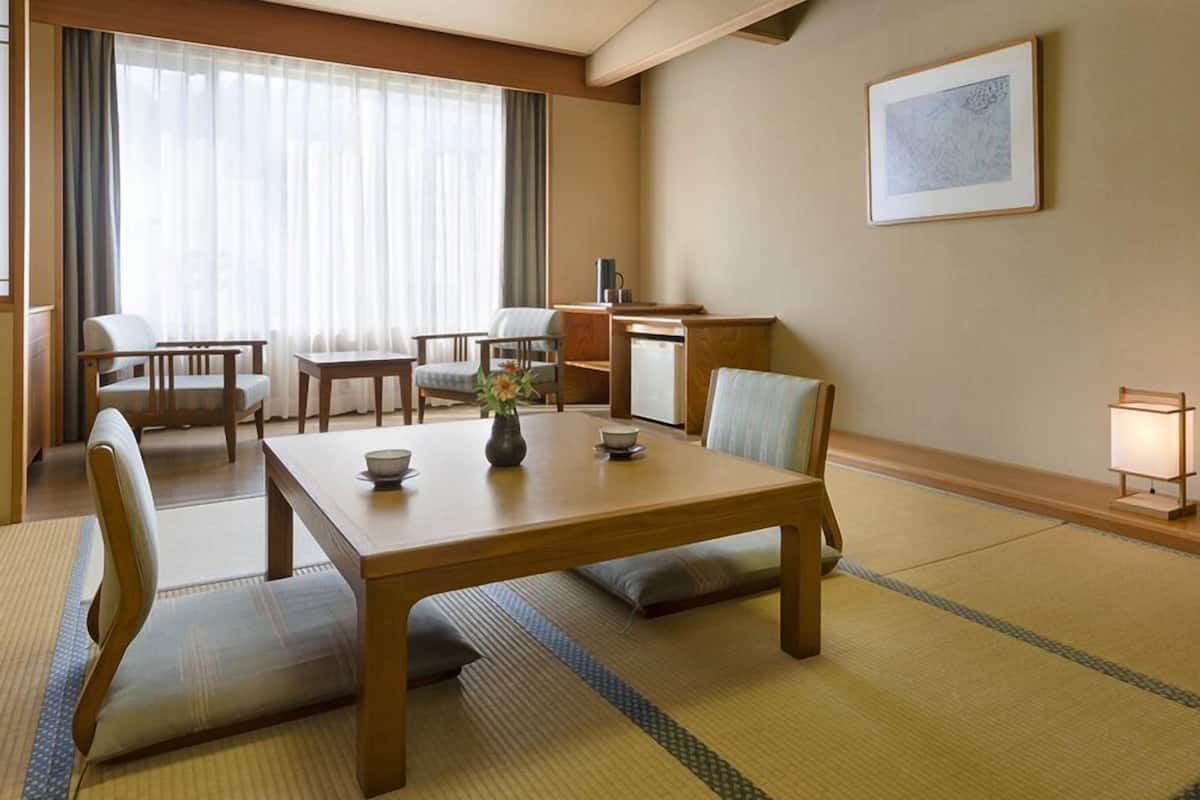 A traditional Japanese-style room with tatami flooring, a low table with a bowl and vase, and a desk with a lamp.
