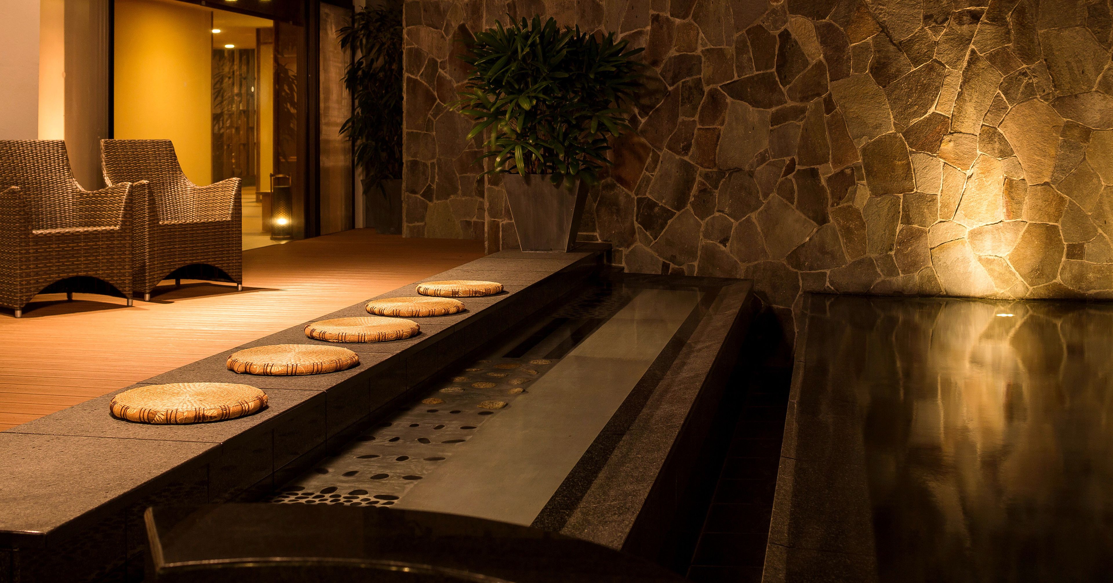 A spa area with stone walls, a water feature, and wicker furniture.