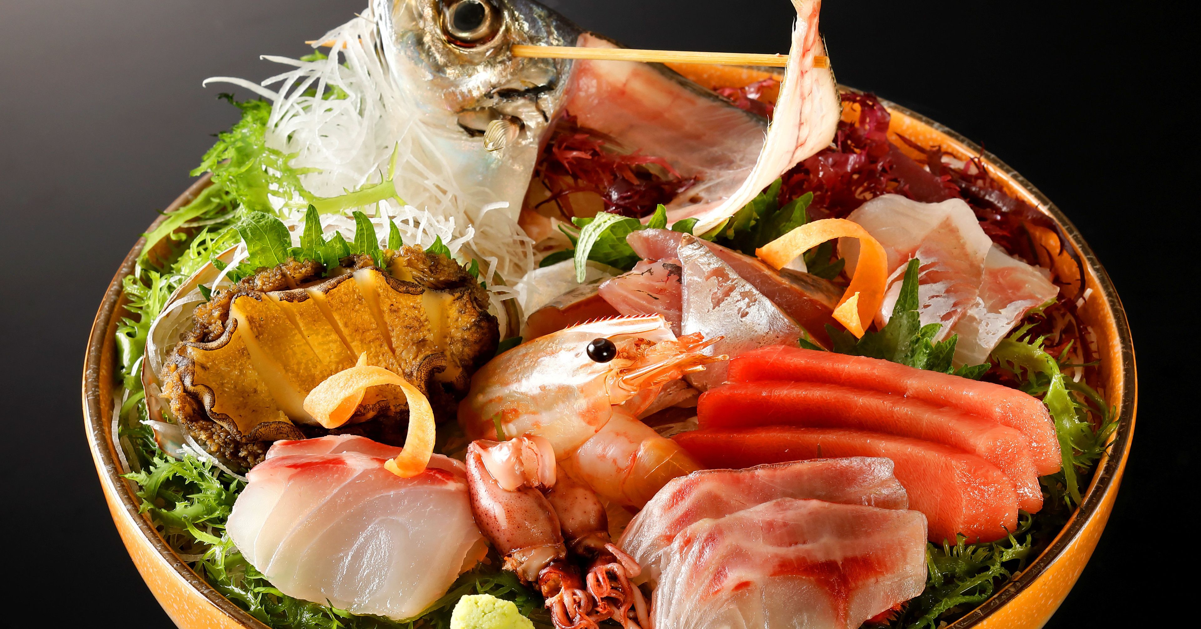 Un bol con mariscos variados, como camarones, pescado y calamares, adornado con verduras y hierbas.