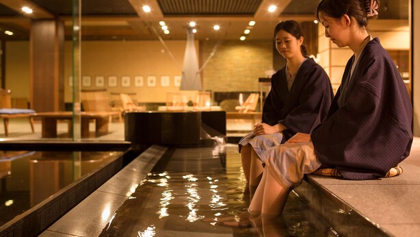 Two individuals seated by a reflective pool in a well-lit indoor setting with a modern design. - Laforet Ito Onsen Yunoniwa (Ito)