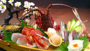 Variedad de mariscos dispuestos en un plato de madera, incluyendo camarones, pescado y otras exquisiteces, con un árbol decorativo y flores al fondo.