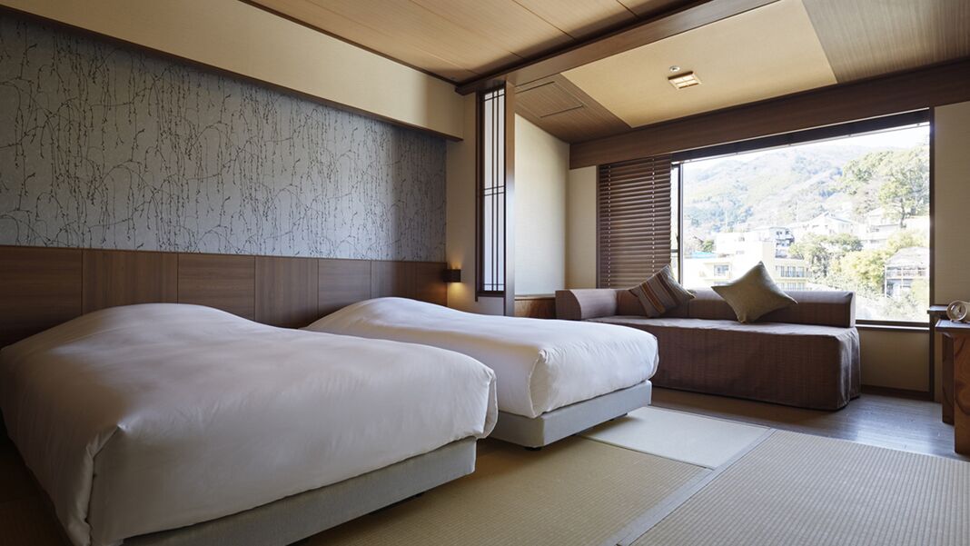 Une chambre d’hôtel avec deux lits, un canapé, une grande fenêtre donnant sur un beau paysage et un plafond en bois.