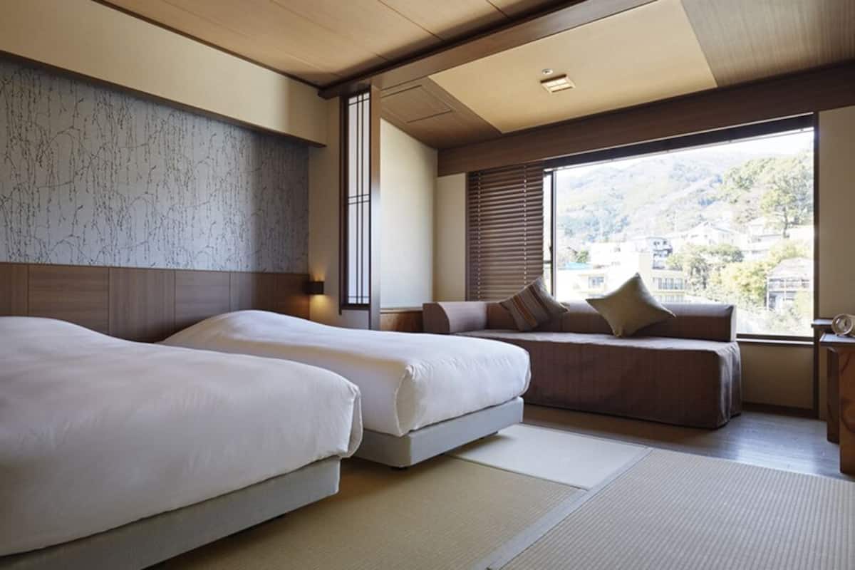 A hotel room with two beds, a sofa, a large window with a view, and a wooden ceiling.
