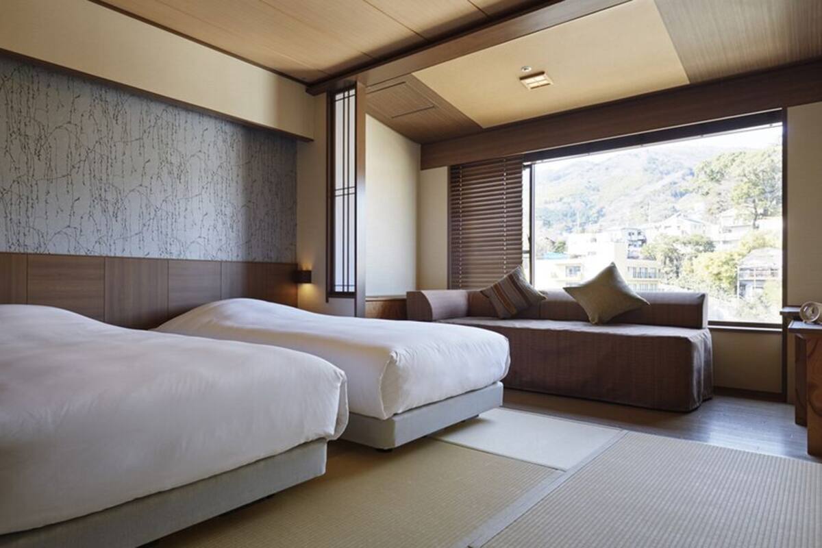 Une chambre d’hôtel avec deux lits, un canapé, une grande fenêtre donnant sur un beau paysage et un plafond en bois.