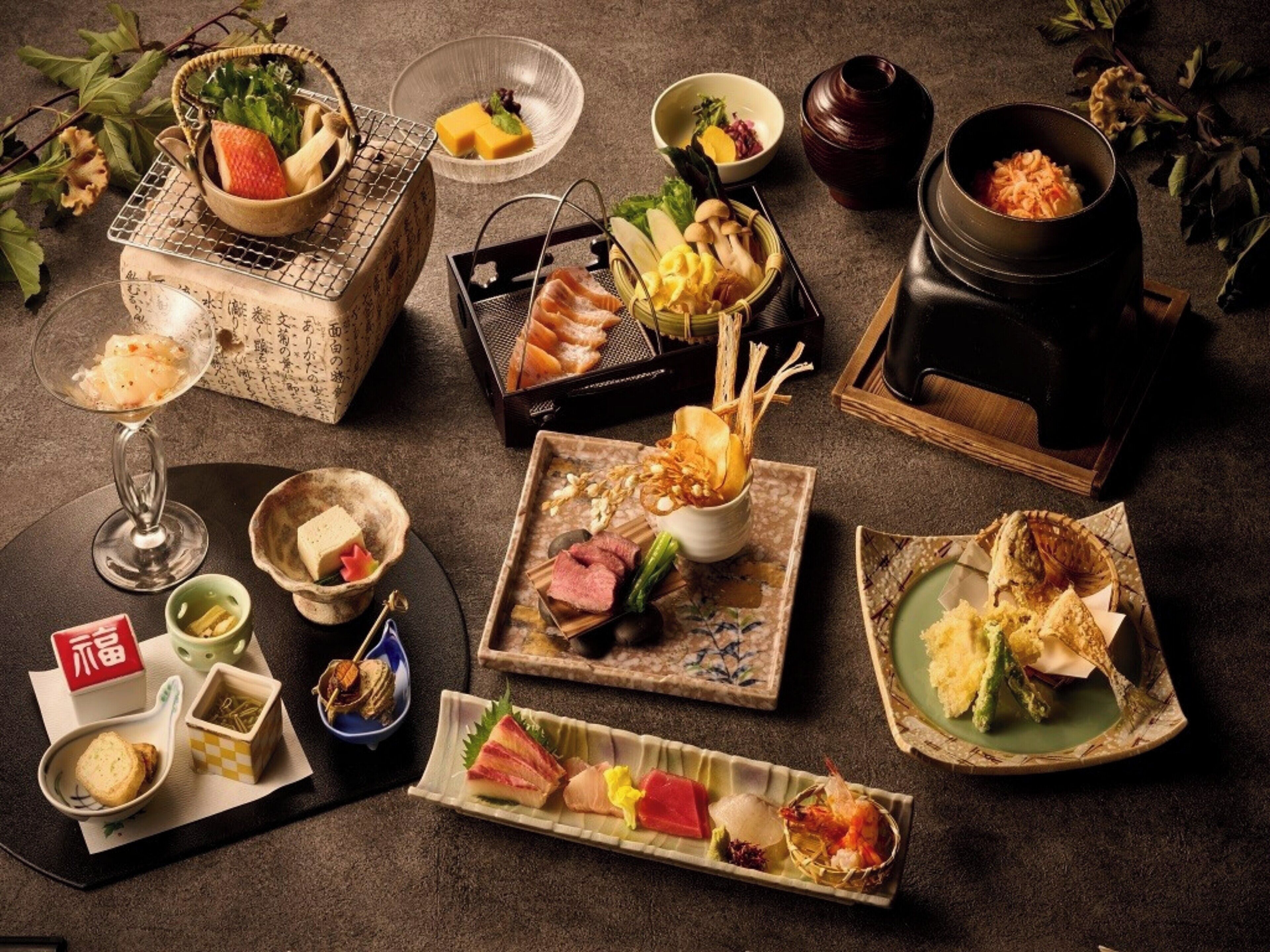 Une variété de plats et de boissons japonais sont disposés sur une table, notamment des sushis, des sashimis et un plat mijoté.