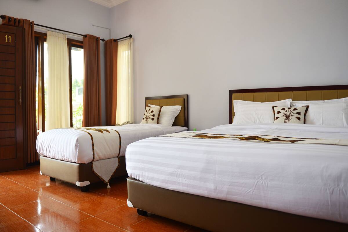 A hotel room with two beds, a wooden door, and a view of greenery outside.