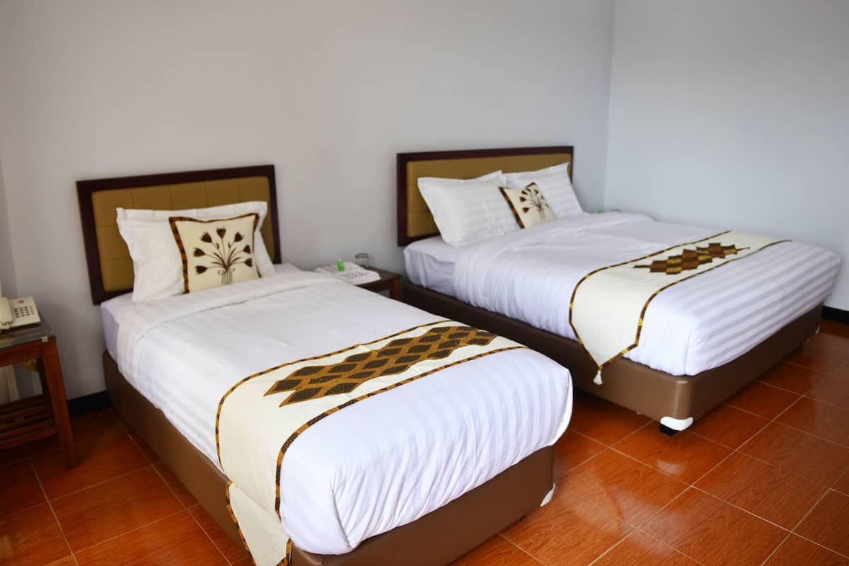 Two single beds with wooden headboards and white bedding, a bedside table with a telephone, and a tiled floor.