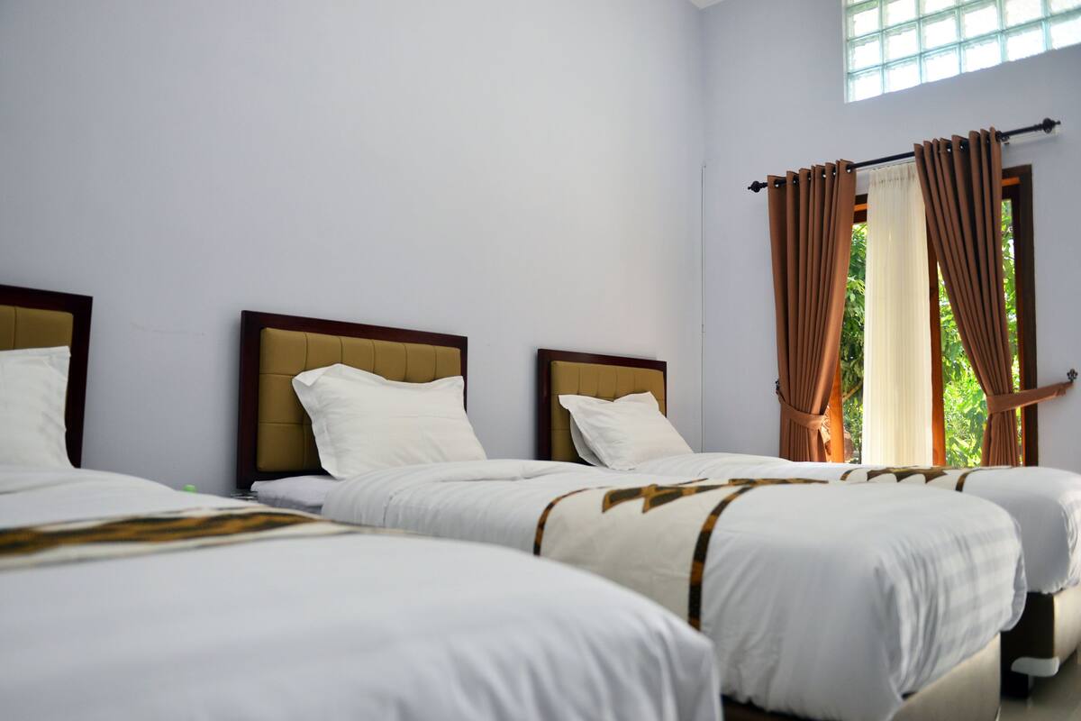 A hotel room with three beds, each with a wooden headboard and white bedding.