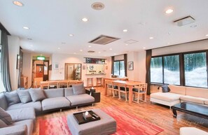 A spacious living area with a sofa, ottoman, and a dining table with chairs. - Morino Lodge Hakuba (Hakuba)
