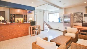 A reception area with a wooden counter, a computer, and a chair. There are wicker sofas and a staircase in the background. - Morino Lodge Hakuba (Hakuba)