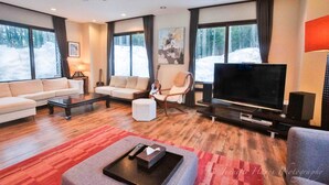A modern living room with a sofa, armchair, and ottoman, a flat-screen TV, and a coffee table. - Morino Lodge Hakuba (Hakuba)