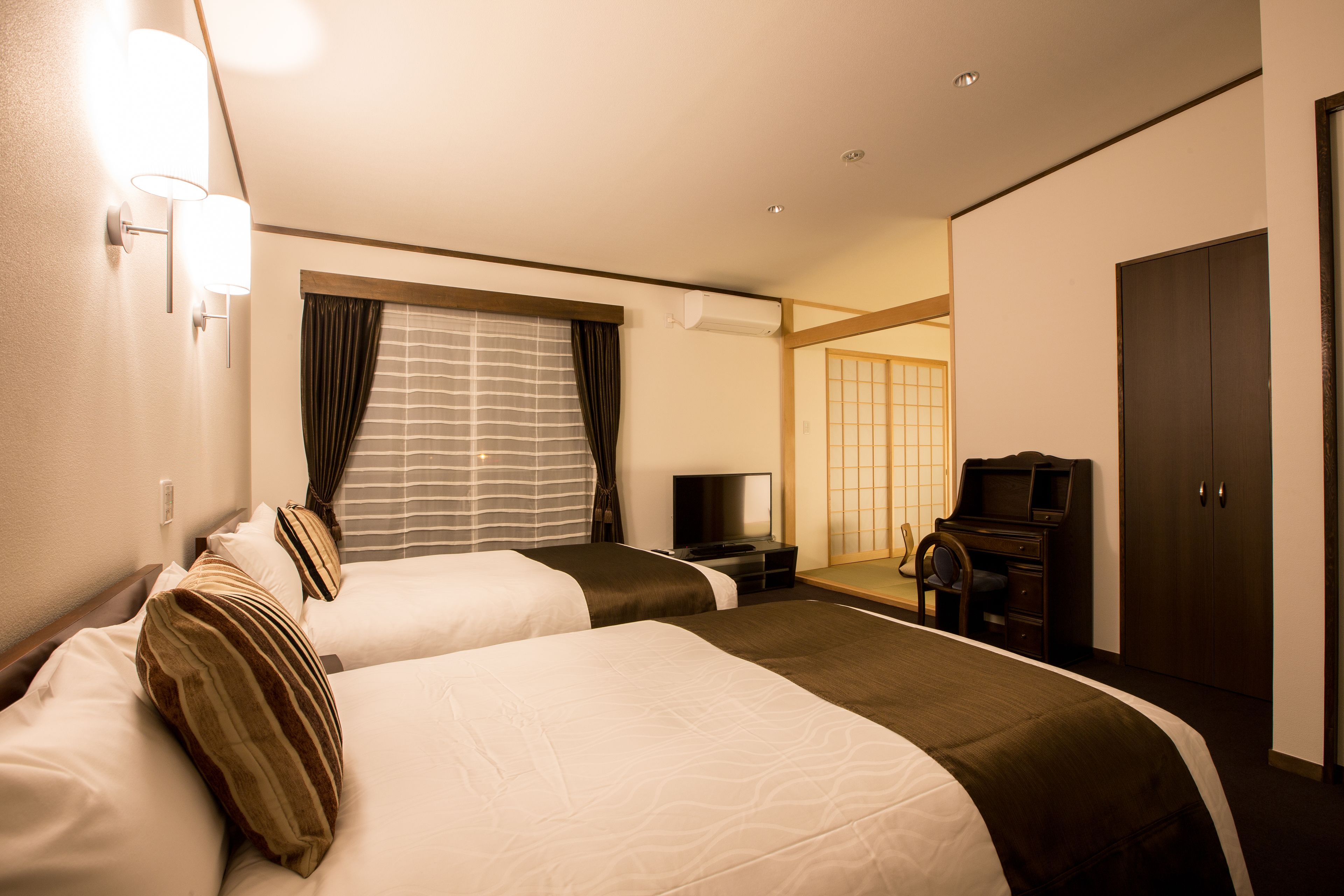 A hotel room with two beds, a TV, a desk, and a wardrobe.