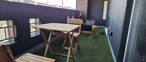 A balcony with a wooden table and chairs, artificial grass, and a view of a mountainous landscape.
