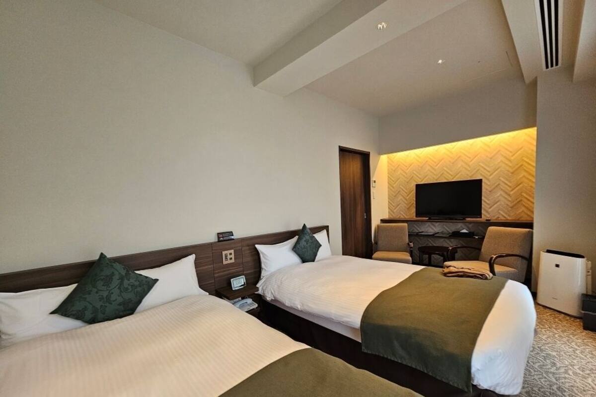 Une chambre d’hôtel avec deux lits, un bureau, une chaise, une télévision et un mini-bar.