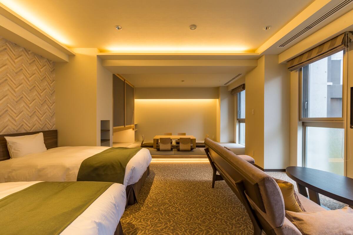 Une chambre d’hôtel avec deux lits, un coin salon et de grandes fenêtres.