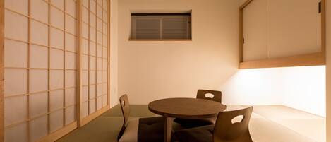 A tatami mat room with a low table and cushions, a sliding door, and a window.