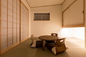A tatami mat room with a low table and cushions, a sliding door, and a window.