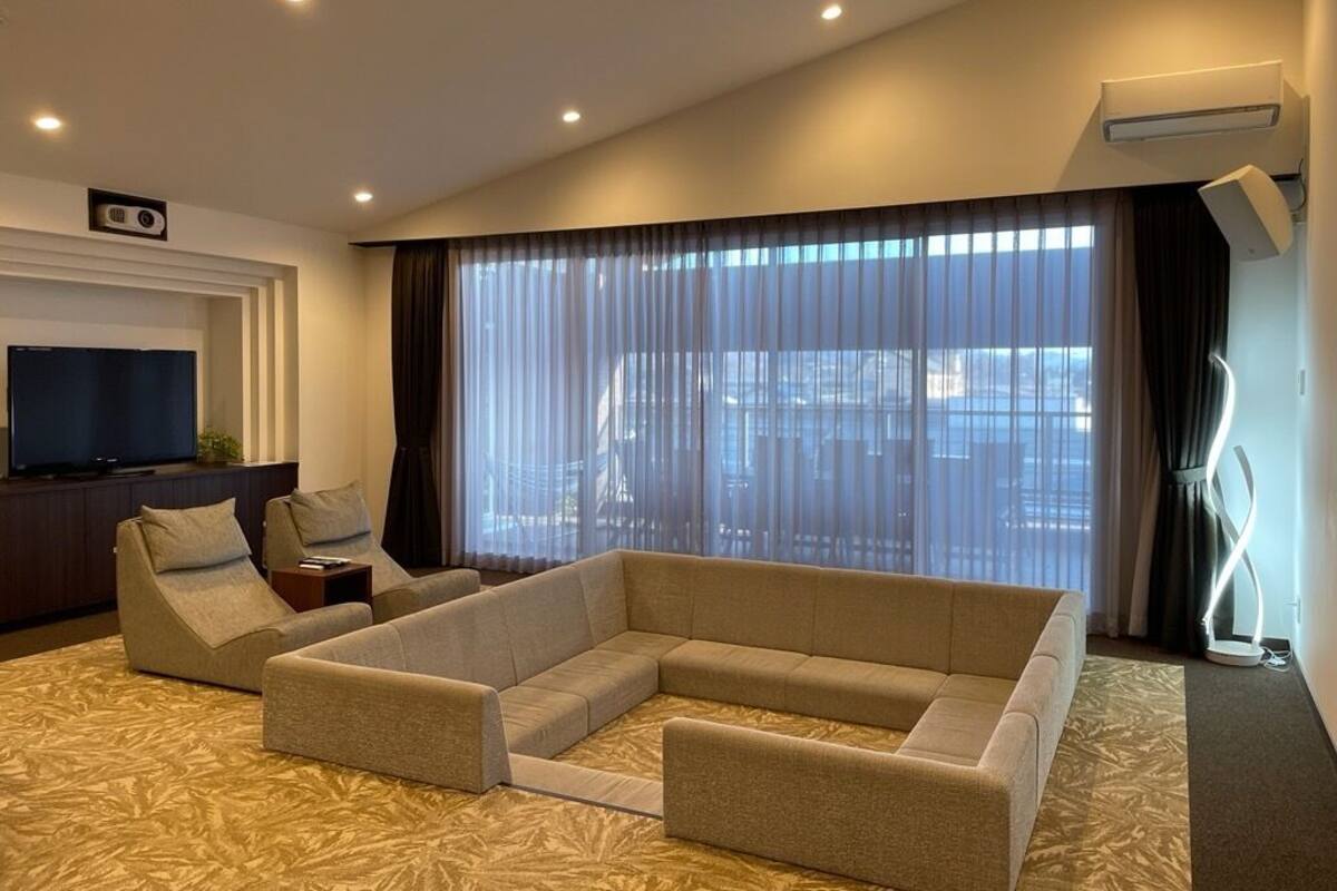 Un salon moderne avec un canapé d’angle, un téléviseur à écran plat et une grande fenêtre agrémentée de rideaux légers.