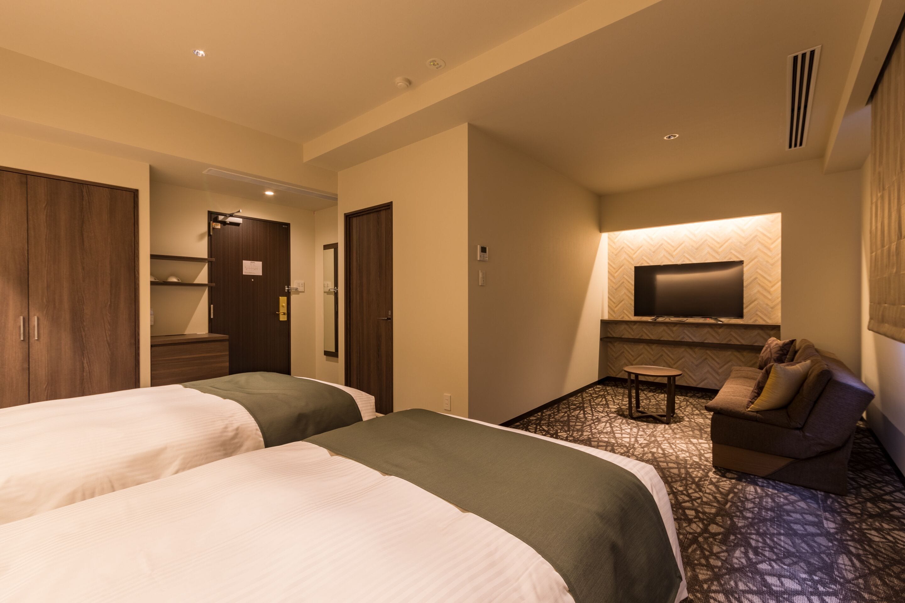 A hotel room with two beds, a sofa, a TV, and a small table.