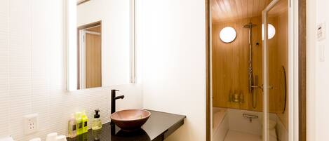 A modern bathroom with a black countertop, a large mirror, a wooden door leading to a shower area, and a basket of towels.