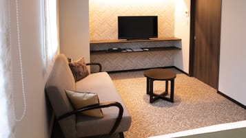 A hotel room with a sofa, a small table, a television on a wooden shelf, and a patterned carpet.