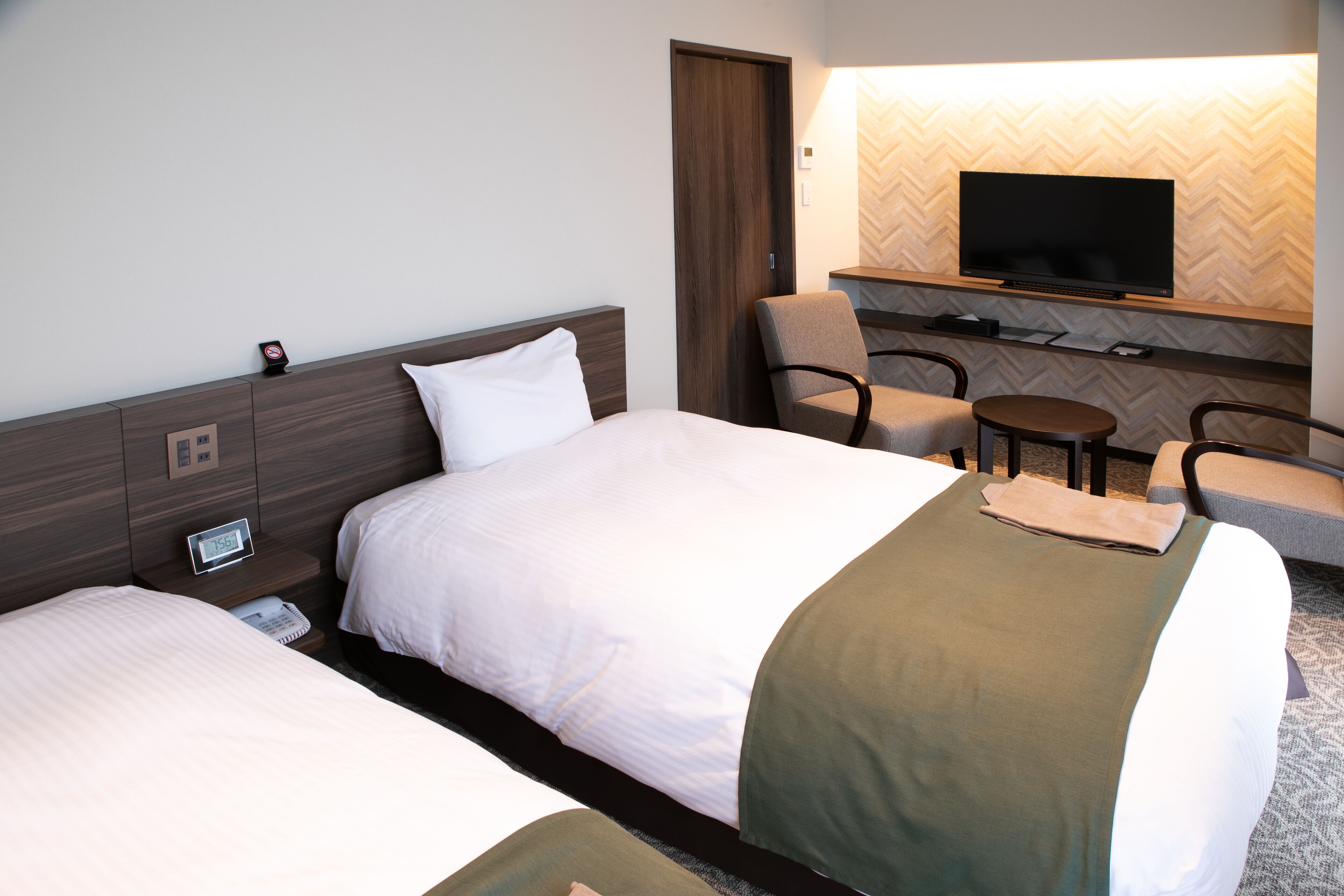 A hotel room with two beds, a TV mounted on the wall, a small table, and a chair.